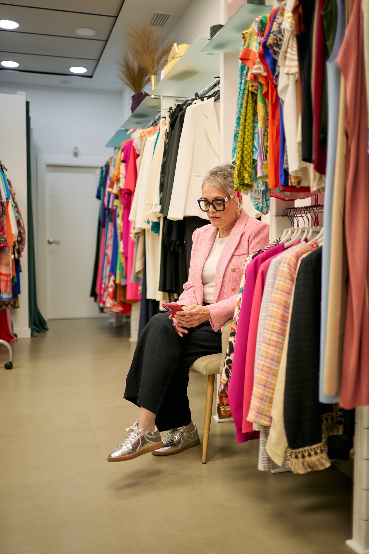 Woman in a pink blazer sitting in a boutique, looking at her phone